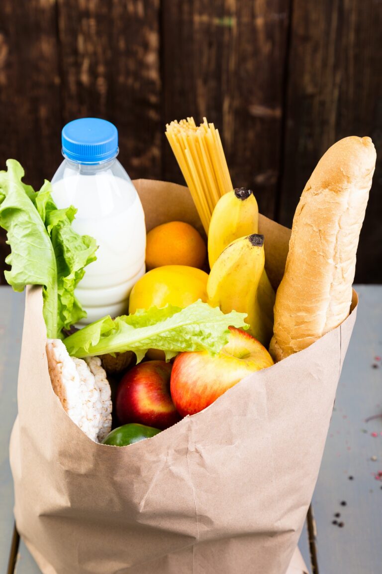 Grocery shopping concept. Different food in paper bag on wooden background.