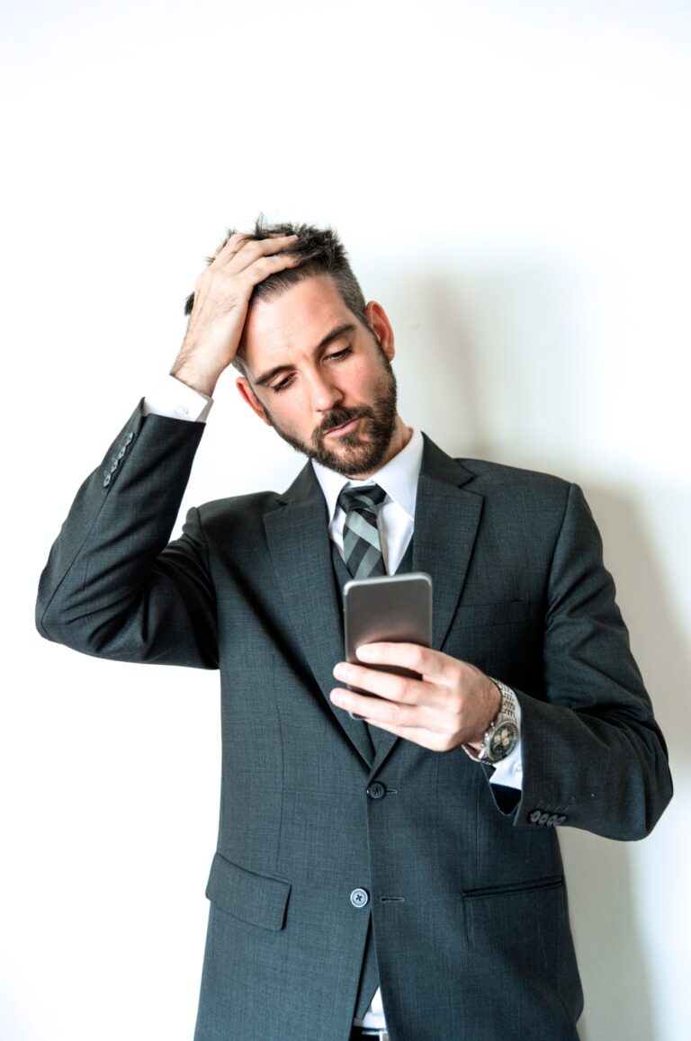 Businessman showing emotion looking at smart phone with hand on forehead.